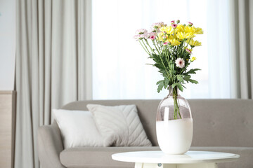 Vase with beautiful flowers on table in living room, space for text. Stylish element of interior design