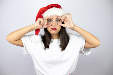 Fototapeta na wymiar Young beautiful woman wearing a christmas hat over white background Trying to open eyes with fingers, sleepy and tired for morning fatigue
