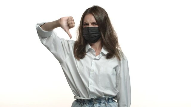 Concept Of Social Distancing, Coronavirus And People. Disappointed Attractive Woman In White Shirt And Medical Mask Saying No, Showing Thumbs-down, Shaking Head In Disapproval, Dislike Something Bad