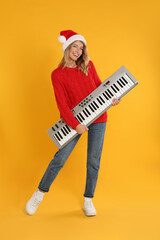 Young woman in Santa hat with synthesizer on yellow background. Christmas music