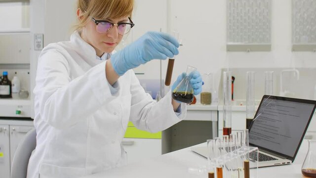 Chemist working with hemp CBD oil in laboratory and writing results in laptop.