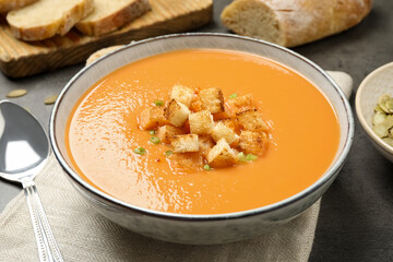 Tasty creamy pumpkin soup with croutons in bowl on grey table