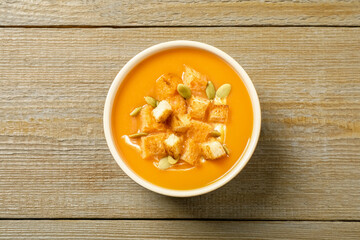 Tasty creamy pumpkin soup with croutons and seeds in bowl on wooden table, top view