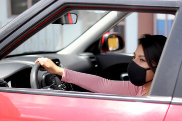 latin woman driver with protection mask inside red car, view in mirror new normal when driving