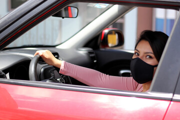 latin woman driver with protection mask inside red car, view in mirror new normal when driving
