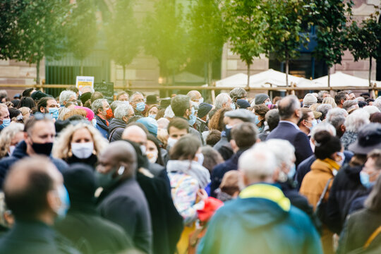 Defocused view of unrecognizable people gathering in the central square during a protest wearing blue surgical protection masks