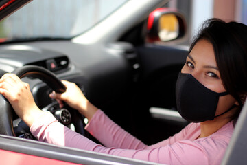 latin woman driver with protection mask inside red car, view in mirror new normal when driving