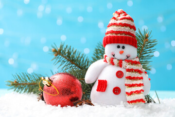 Cute toy snowman, fir branch and Christmas ball on snow against blurred background