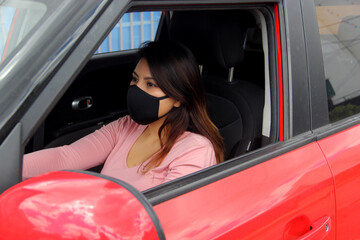 latin woman driver with protection mask inside red car, view in mirror new normal when driving