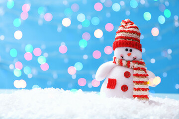 Cute snowman in snow against light blue background, bokeh effect. Space for text