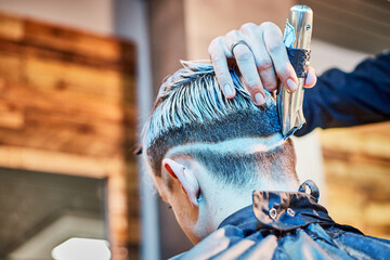 Close-up of hairdresser’s hand adjusting haircut with electric razor from the back. Barbershop...