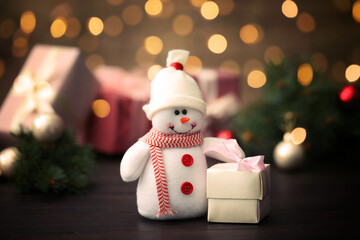 Cute snowman with gift on table, bokeh effect