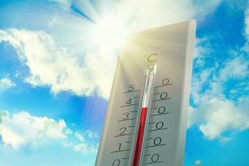Weather thermometer showing high temperature and blue sky with clouds on background