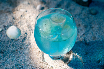 blue cocktail with ice on sand background with sea shells