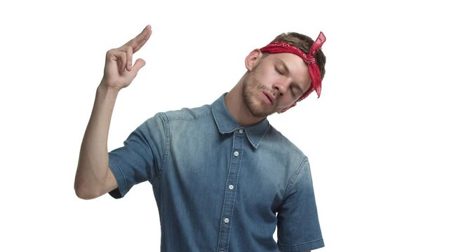Sassy handsome guy with beard, red bandana over forehead, making finger gun sign over head and shooting himself with unamused and bored expression, standing over white background