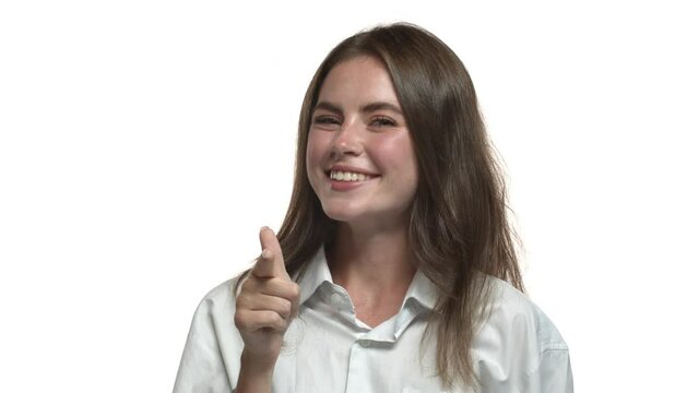 Close-up of pleased pretty woman in casual shirt, pointing finger at camera and nodding in approval, make gotcha gesture, standing against white background