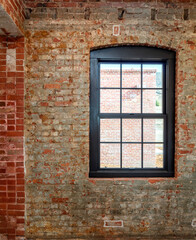 old red brick wall with window with curved brick arch, shot from inside building looking out window