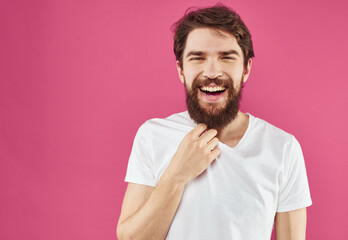 Obraz premium A cheerful guy with a beard laughs on a pink background and gestures with his hands