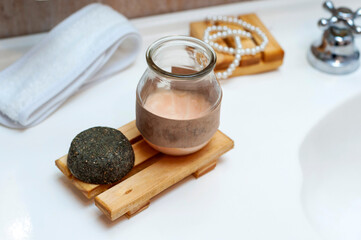 Modern and ecological wooden soap holder on a bathroom counter, with soap and shampoo in a bottle along with a reusable cleaning pad. for body care