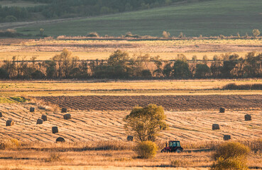 Fototapeta na wymiar Lonely tractor harvest hay field crop stubble golden yellow orange autumn mountain background massive bulgaria technology machine agriculture