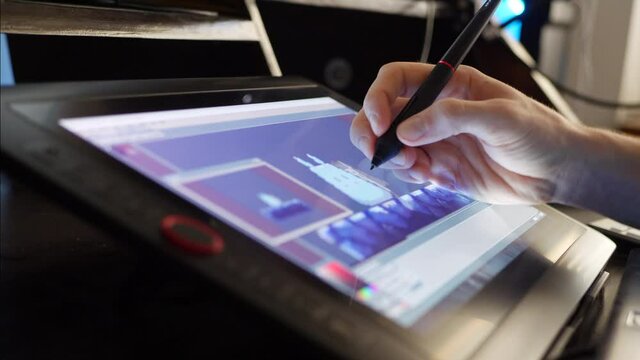 A digital artist creating retro pixel art in a video game development studio on a touch screen drawing tablet with stylus pen.