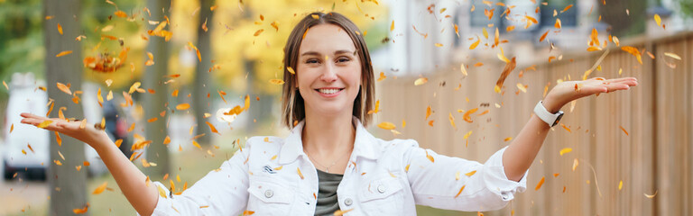 Happy middle age Caucasian woman throwing autumn fall yellow leaves. Young woman with short haircut...