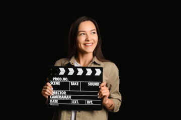 Young female film director with movie clapper on dark background