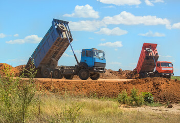 Two Dump Trucks pour soil from bodies