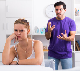 Obraz premium Upset young woman sitting at home table with disgruntled man behind