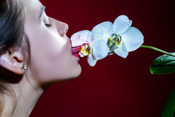 Sexy girl lick orchid flower. Orchids oral tongue. Sensual young woman suck floral orchidea. Red lirs with lipstick. © Volodymyr