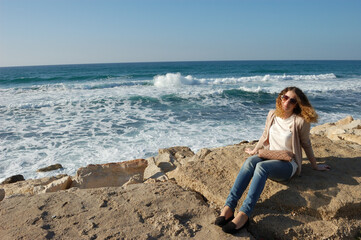 Fototapeta na wymiar young curly girl in jeans, glasses, surf rocks on vacation by the sea, tourism