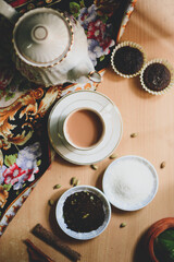 Cup of masala tea with ingredients e.g. tea leaves, cinnamon, cardamom, sugar and tea cakes