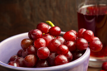 Refreshing Ripe fresh red, purple grapes in a ceramic bowl with a glass of grape juice on wood background