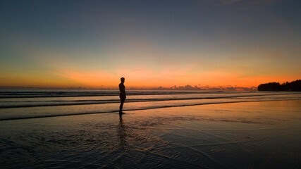 Fototapeta premium young man standing on the beach with a beautiful sunset
