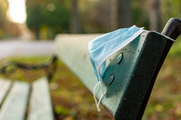 Health care and protection from COVID-19 concept, A piece of blue surgical mask hanging on a park bench after use, Waste procedure or medical mask.