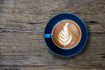 Top view of Latte hot coffee (or cappuccino) in a blue cup with latte art and roasted coffee beans on wooden table background
