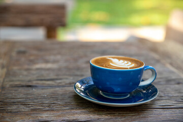 Latte hot coffee (or cappuccino) in a blue cup with latte art and roasted coffee beans on wooden table at cafe shop background
