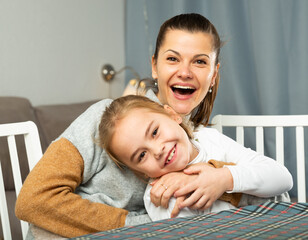 Happy woman laughing and tickle her daughter in home interior