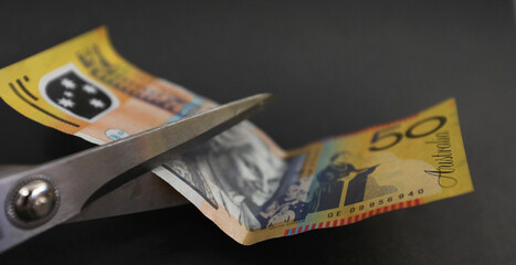 Australian 50 fifty dollar note about to be cut with scissors. tax cut saving spending cuts divorce...