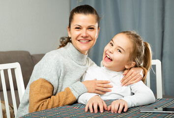 Young mother laughing and tickle her small daughter at sofa at home