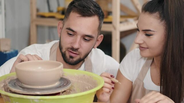 Loving couple carving on the pottery pot. Couple's faces closeup. Pottery’s workshop. Man helps woman to make a pottery pot. Love story in pottery’s workshop surroundings.