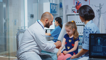 Obraz premium Medical practitioner bandaging child injured arm sitting in bed. Healthcare physician specialist in medicine providing health care service radiographic treatment examination in hospital cabinet.