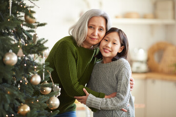 Fototapeta premium Portrait of Asian mother embracing her daughter standing near the Christmas tree they smiling at camera