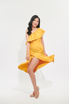 Portrait of laughing young woman in yellow dress swirling and dancing isolated on white background