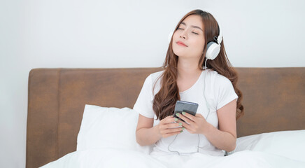 Beautiful young asian woman with headphones relaxing on the bed. She is listening to music using...