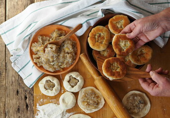 An elderly woman is preparing a healthy lunch. Ready made belyashis with ingredients for their preparation on a kitchen board on a wooden background.