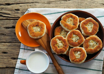 Country style. Freshly baked homemade belyashi, in a plate on a wooden background with a wooden kitchen spatula and a cup of milk. Healthy natural food.
