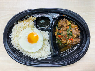 Rice topped with stir-fried beef and basil with fried egg in the food container