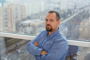 A confident young man looks at the camera. Happy handsome guy stands at the window, thinking about...