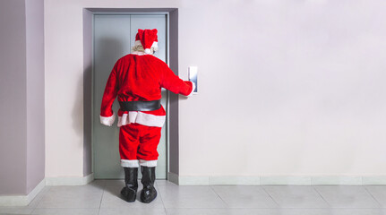 Man in Santa Claus costume calls elevator in building at Christmas - obrazy, fototapety, plakaty